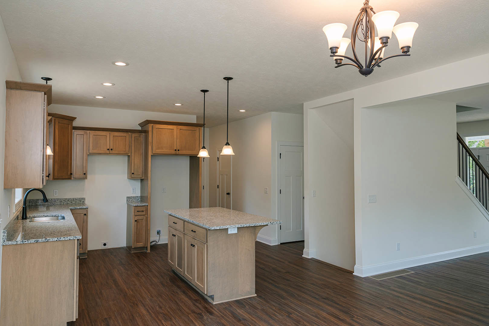 Marble kitchen island with waterfall edge, wood plank flooring, white cabinetry, stainless steel appliances, and modern chandelier overhead