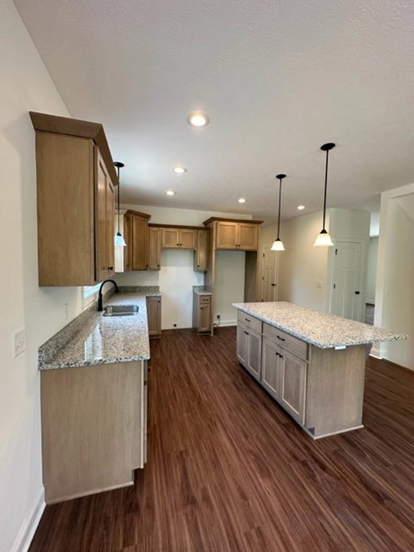 Granite countertops, wood cabinetry, and polished wood flooring in a modern kitchen with stainless steel sink and neutral walls