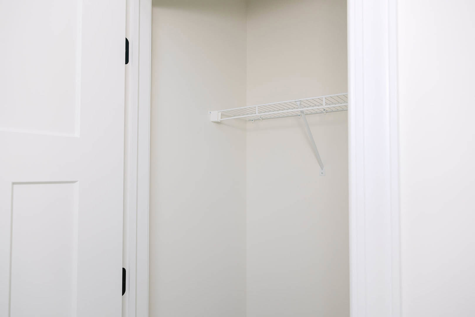 White closet interior with a built-in shelf and white door featuring a silver handle, smooth painted walls, and minimal trim detailing.