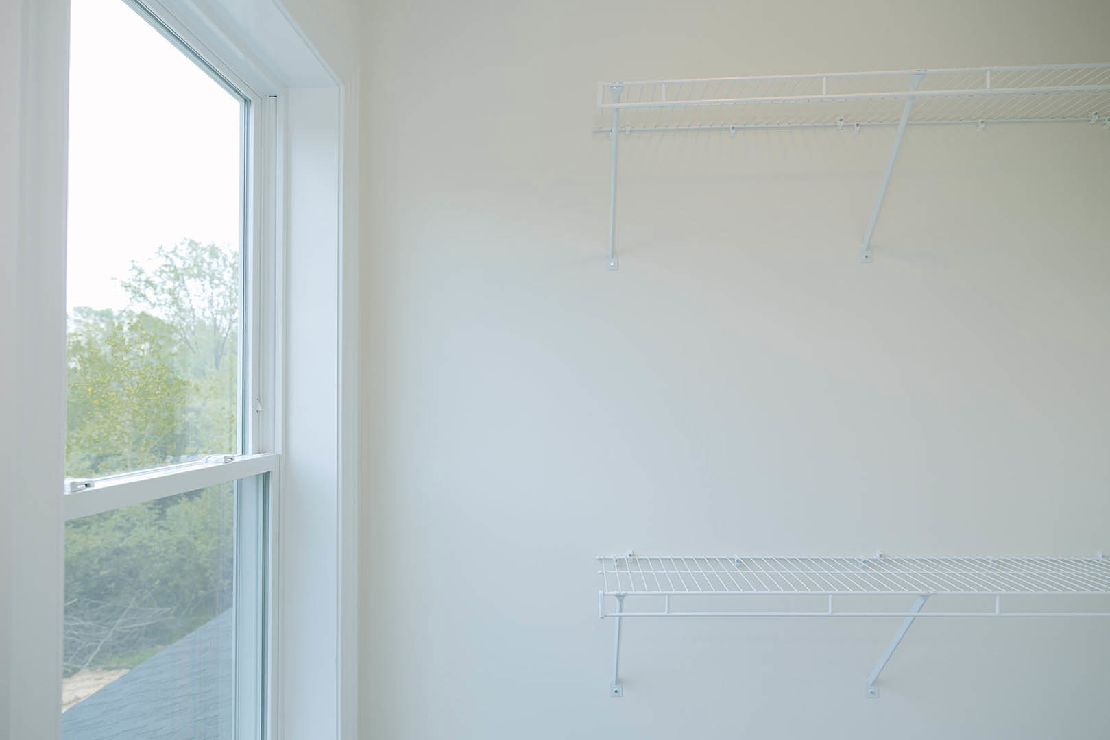 White floating shelf mounted on plaster wall beside rectangular window with view of green trees outside, interior of custom home in Ohio
