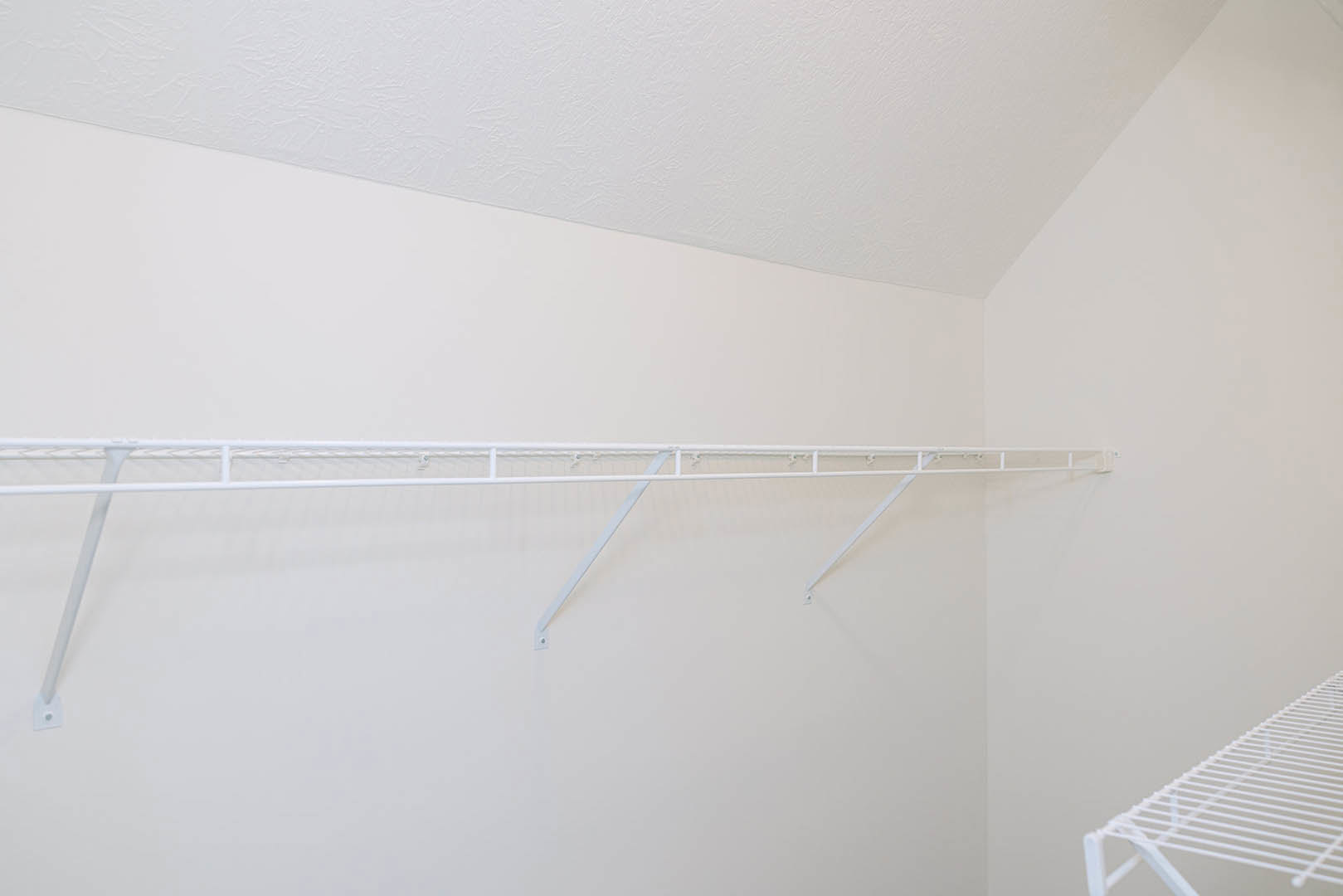 White metal clothes rack mounted on a plaster wall beneath a white ceiling, featuring hooks and a shelf for storage.
