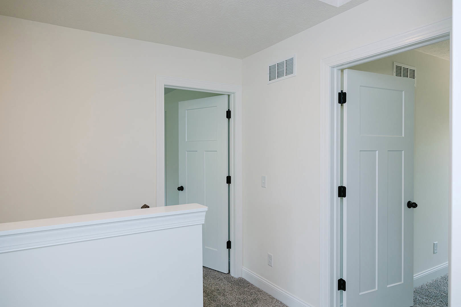 White room with two white doors featuring black handles, smooth plaster walls, ceiling molding, and a row of wall ventilators.