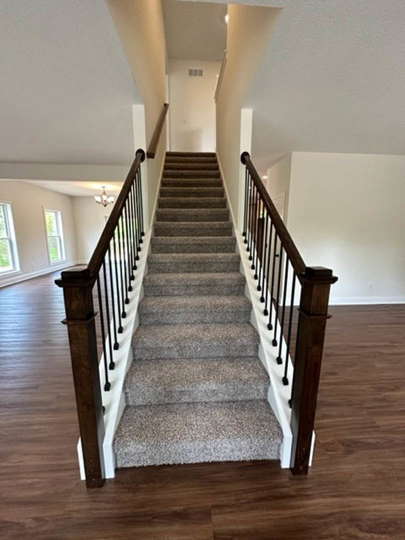 Carpeted staircase with wooden handrail and balusters, laminate flooring, two windows, and ceiling light fixture in a residential interior