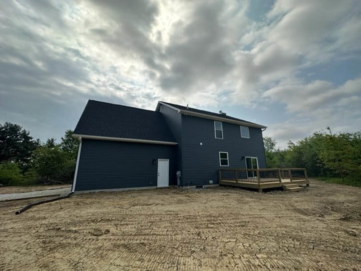 Wooden deck with railing attached to a house featuring a white door with black knobs, dirt yard in foreground, cloudy sky above