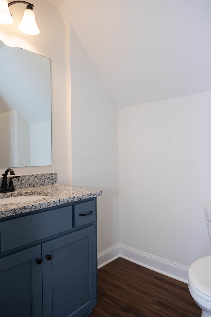 Marble bathroom countertop with chrome faucet, large framed mirror, dark wood flooring, white baseboards, and white walls