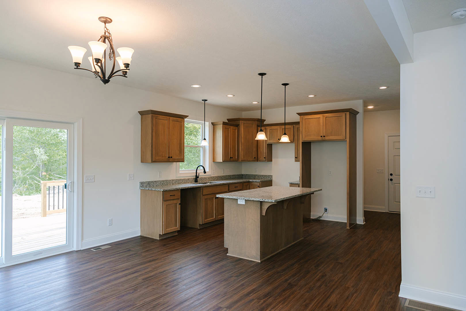 Kitchen with dark wood flooring, granite island countertop, white cabinetry, glass door opening to outdoor view, chrome faucet, and ornate chandelier hanging from ceiling