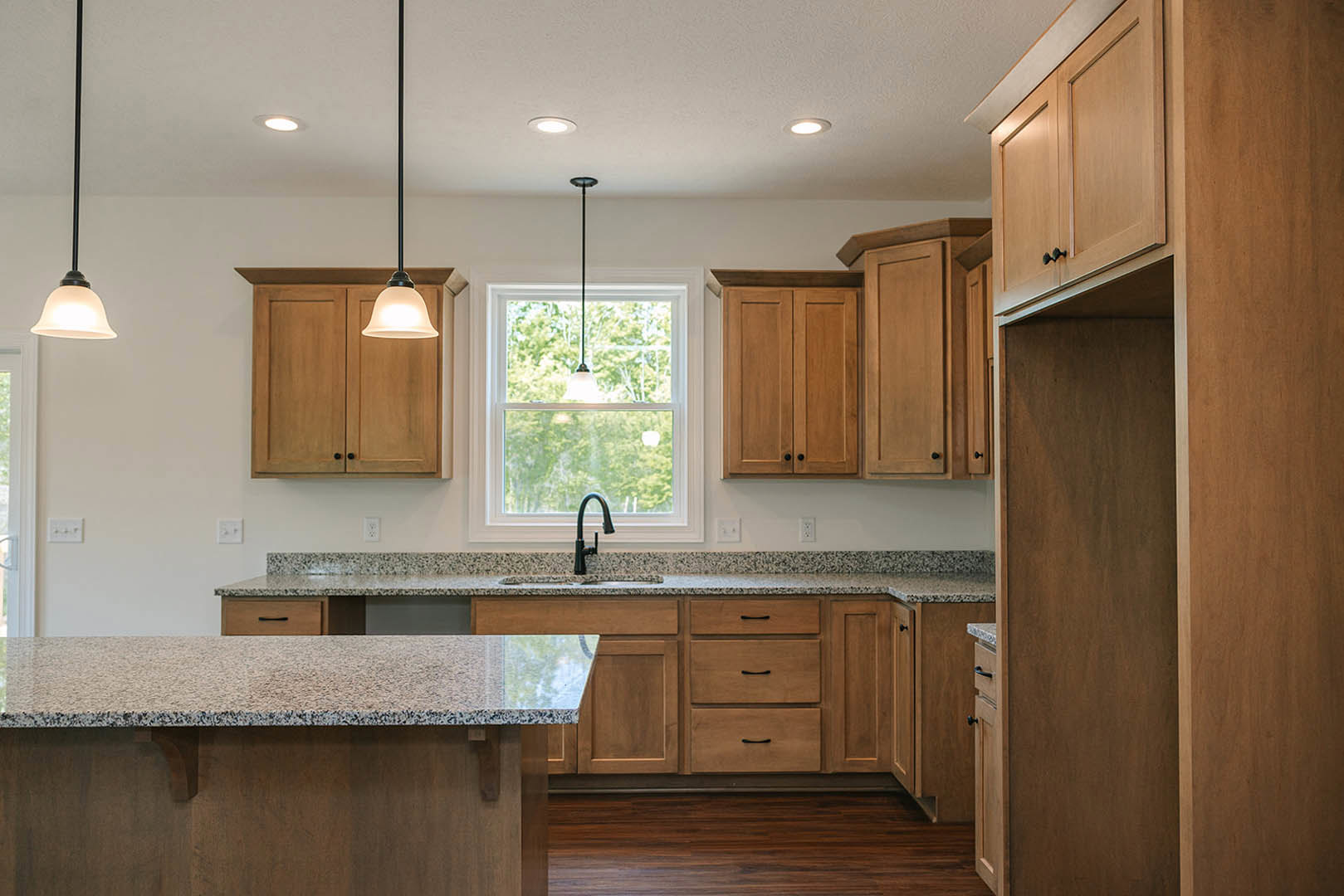 Granite countertops, wood cabinets, stainless steel faucet, pendant ceiling light, hardwood flooring, open drawer in custom kitchen