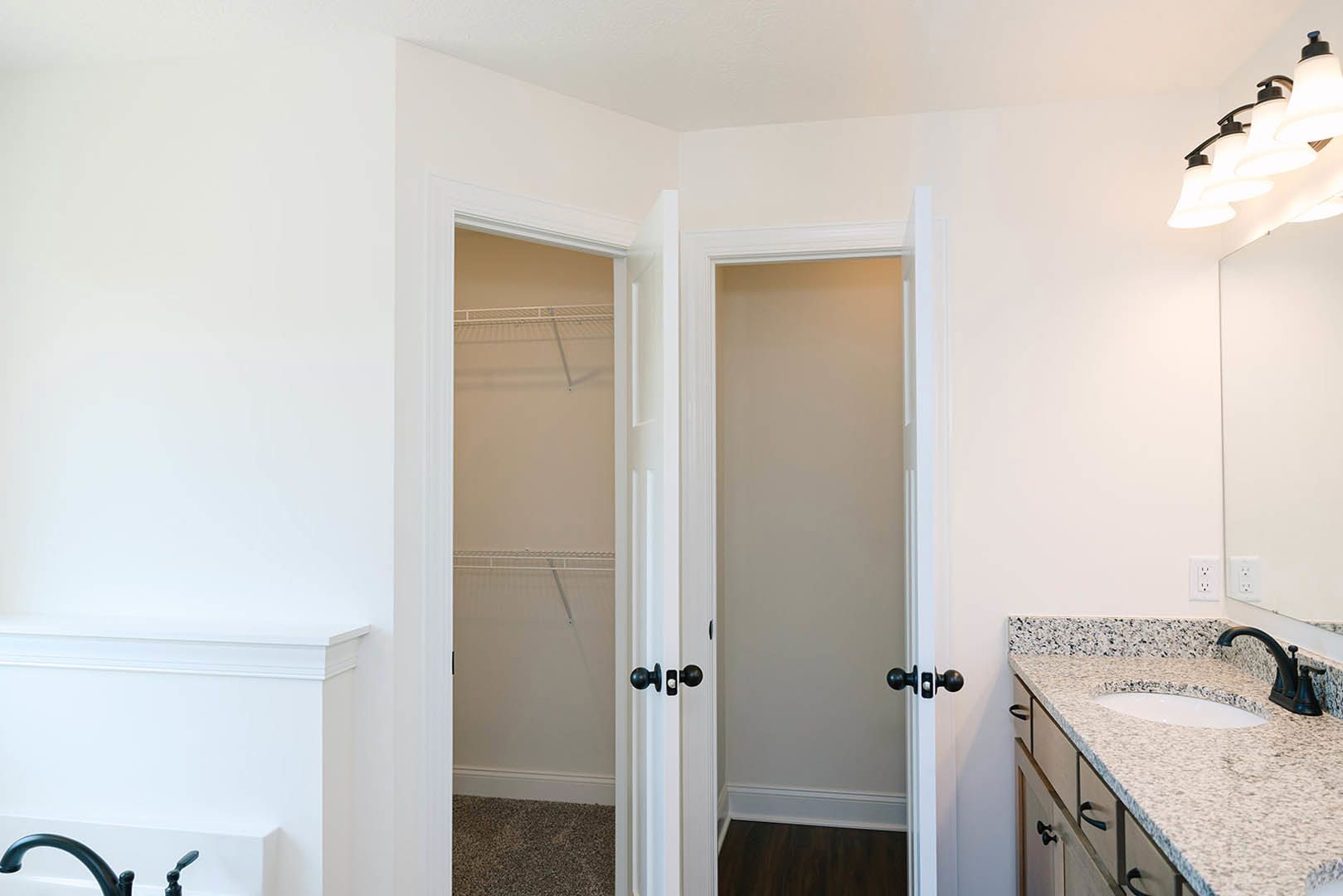 White closet with black handles beside a white oval sink with black border, tile flooring, and built-in shelving against a white wall.
