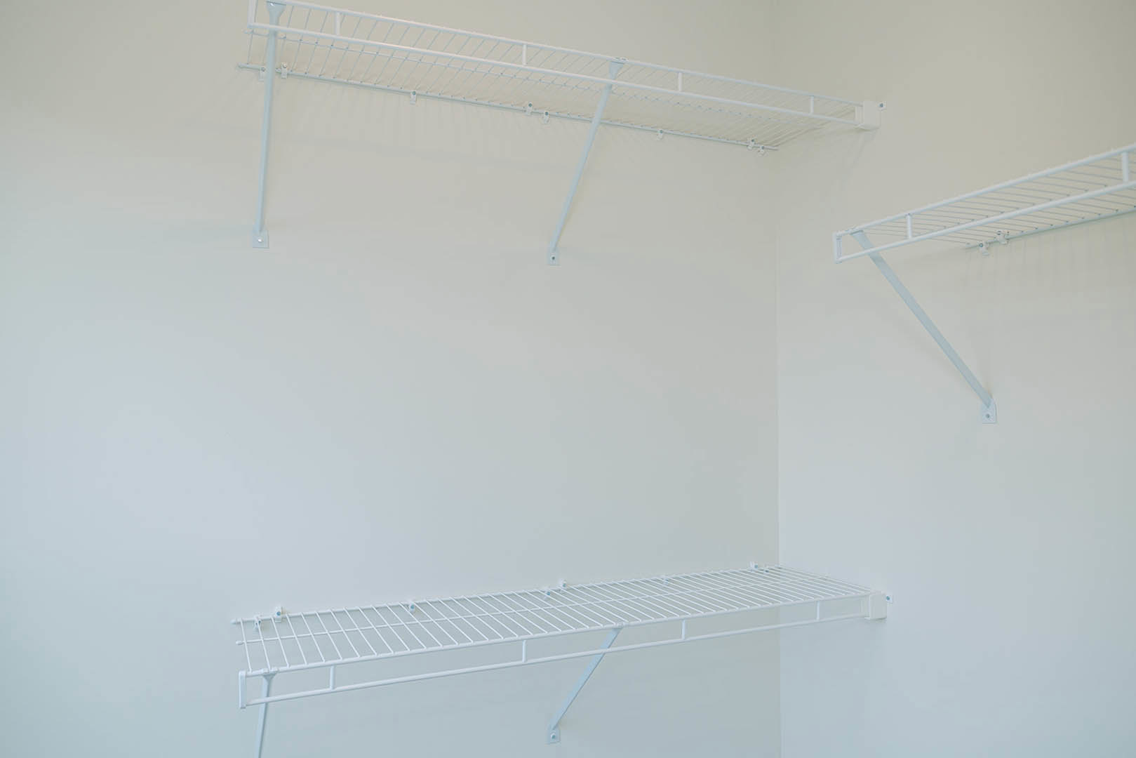 White built-in shelves mounted on a smooth white wall, adjacent to a white ceiling with exposed beam and pipe.