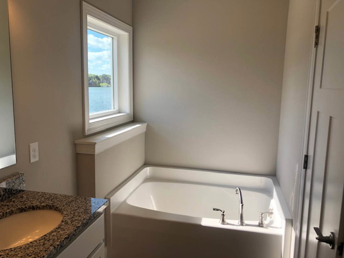 Modern bathroom featuring a freestanding white bathtub with chrome faucet, rectangular sink set in a stone countertop, tiled walls, wall-mounted outlet, and partial view of a