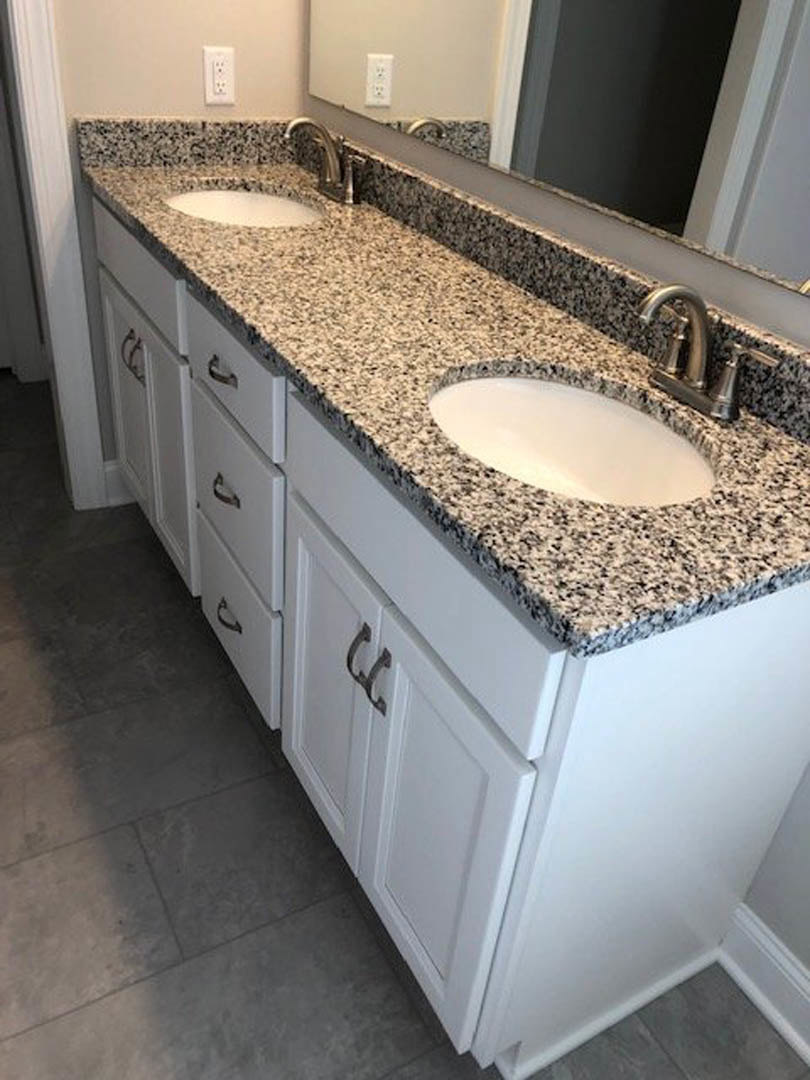 Granite bathroom countertop with white oval sink, chrome faucet, light tile backsplash, and wood cabinetry