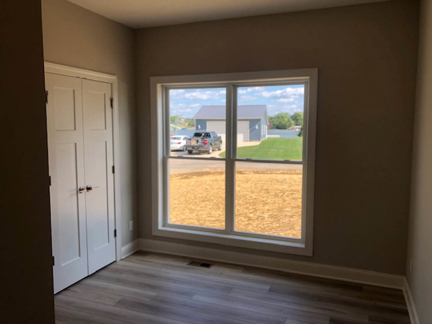 Sunlit room with large window, natural wood flooring, white walls, and partial view of a door