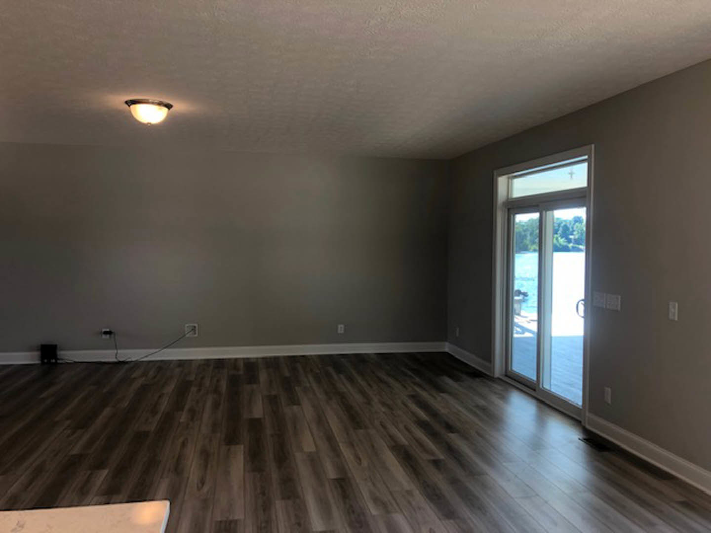 Wood flooring with white trim, large window overlooking water and trees, white wall with a square accent, black box near doorway