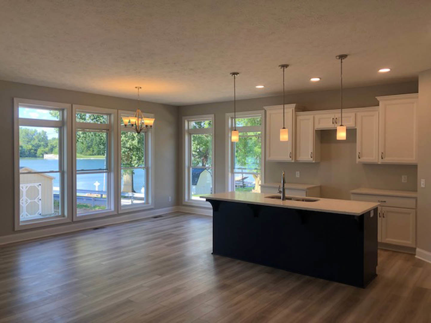 Kitchen with black countertop island and sink, wood flooring, white tile backsplash with black accents, multiple large windows, cabinetry, and a chandelier.