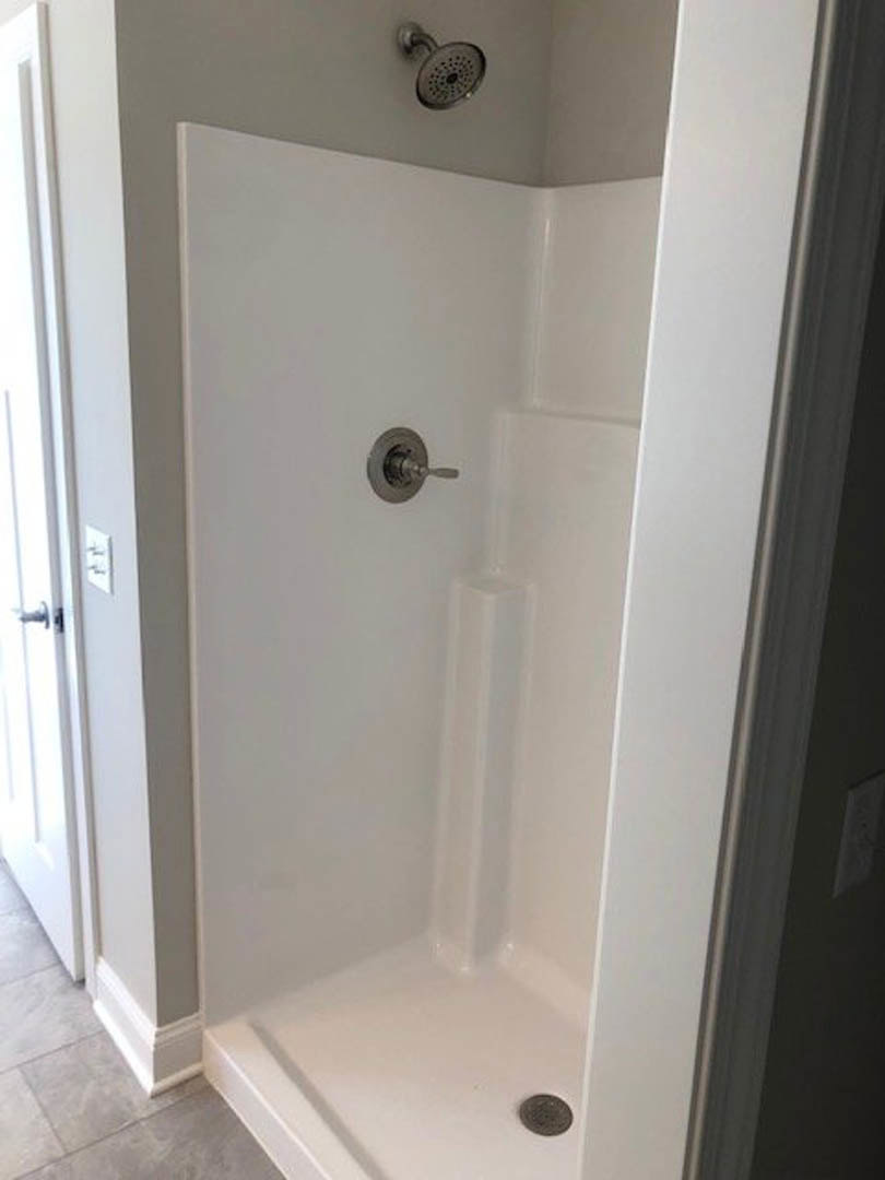 Modern bathroom shower with round chrome showerhead, silver handle, white tiled walls, and built-in plumbing fixtures