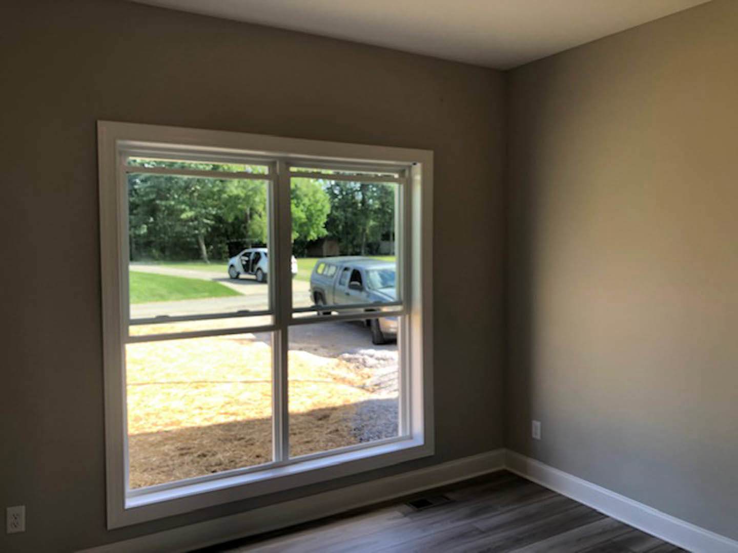 Sunlit room with light-colored walls, large window with blinds, white electrical outlet, and a silver truck parked outside