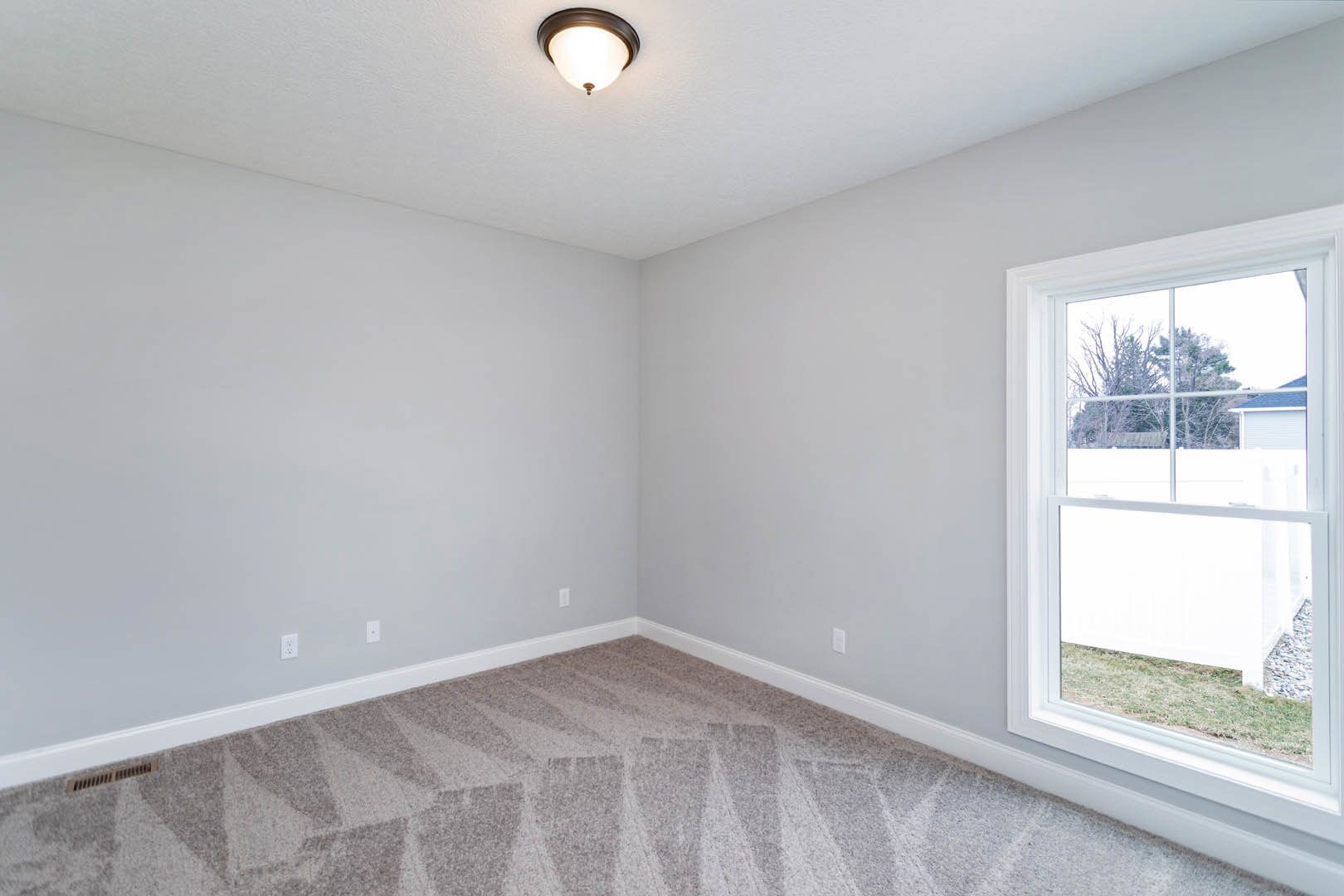 Carpeted room with white walls, ceiling light fixture, large window overlooking neighboring house and trees, decorative molding along ceiling edges