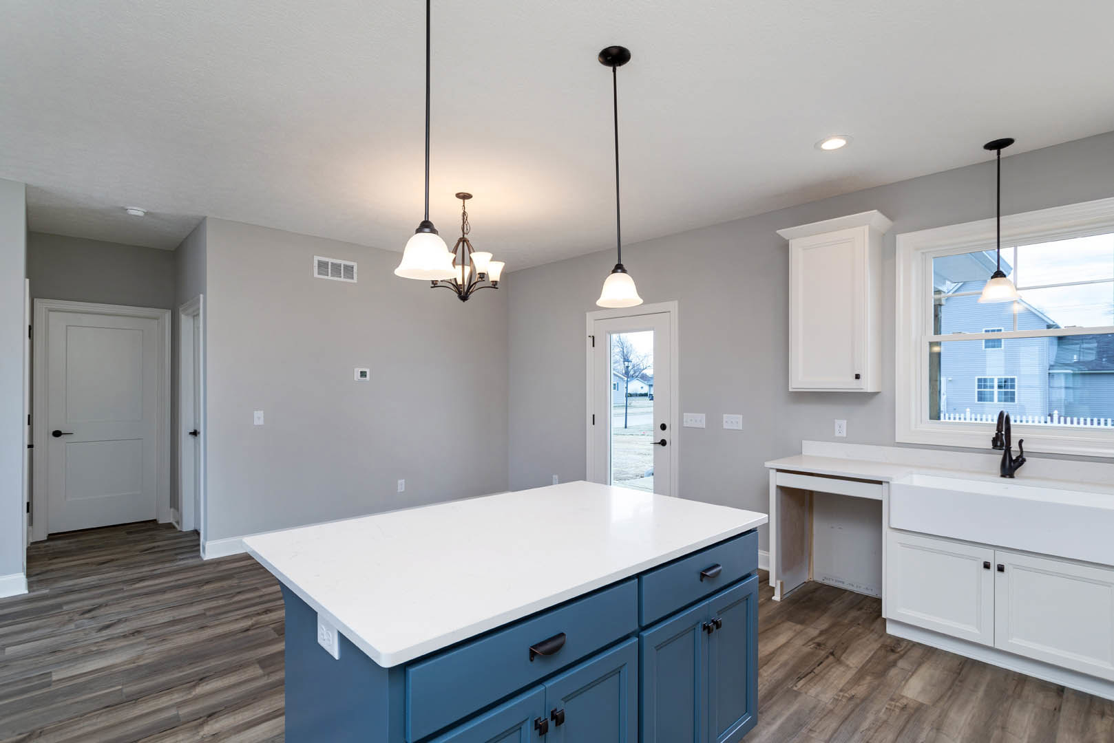 Kitchen featuring white quartz countertop, blue shaker cabinets, undermount sink, pendant chandelier, white door with black handle, light wood flooring