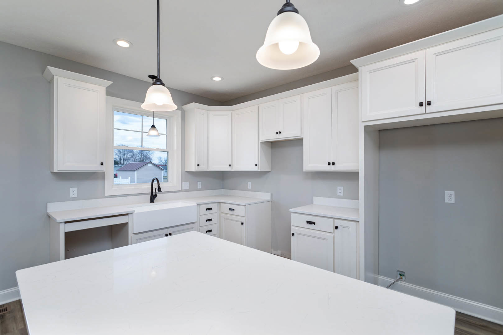 White kitchen with shaker cabinets, quartz countertop, stainless steel faucet, pendant light with white shade, and window above sink