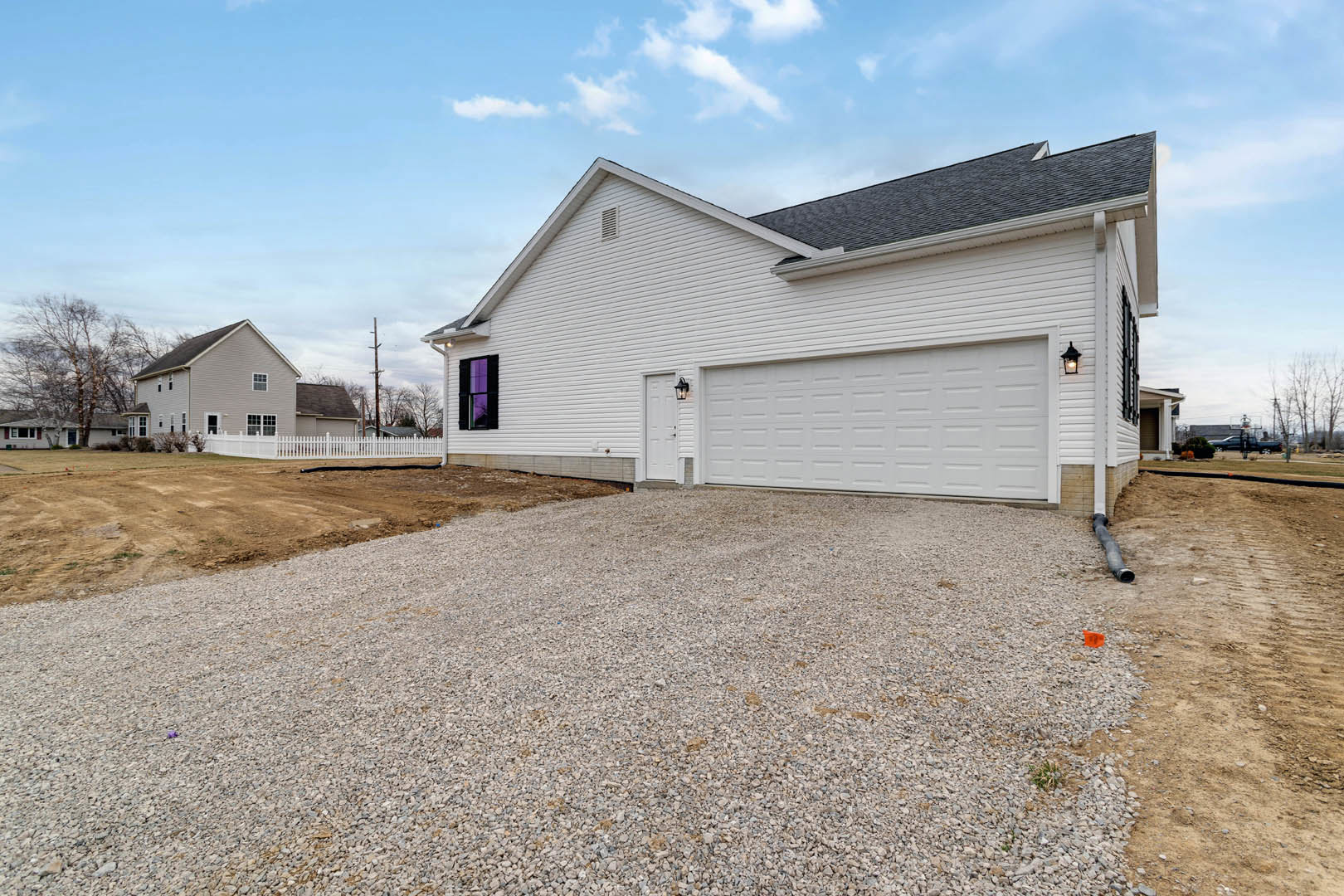 White house with gravel driveway, white garage door, purple glass window, white fence, and close-up of shingled roof under partly cloudy sky