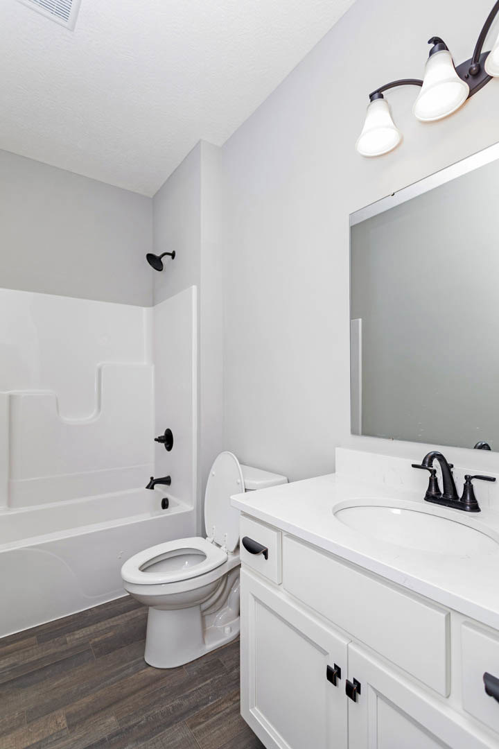 White bathroom featuring a freestanding bathtub, toilet with seat up, modern sink with chrome faucet, light fixture above, and tiled walls.