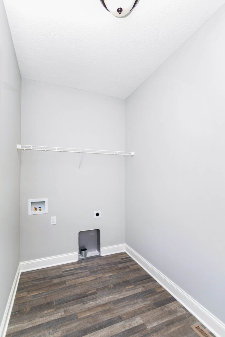 Wood floor room with white walls, small hole near baseboard, metal trash can on white shelf, white box with two water taps, close-up of ceiling light bulb, rectangular white object