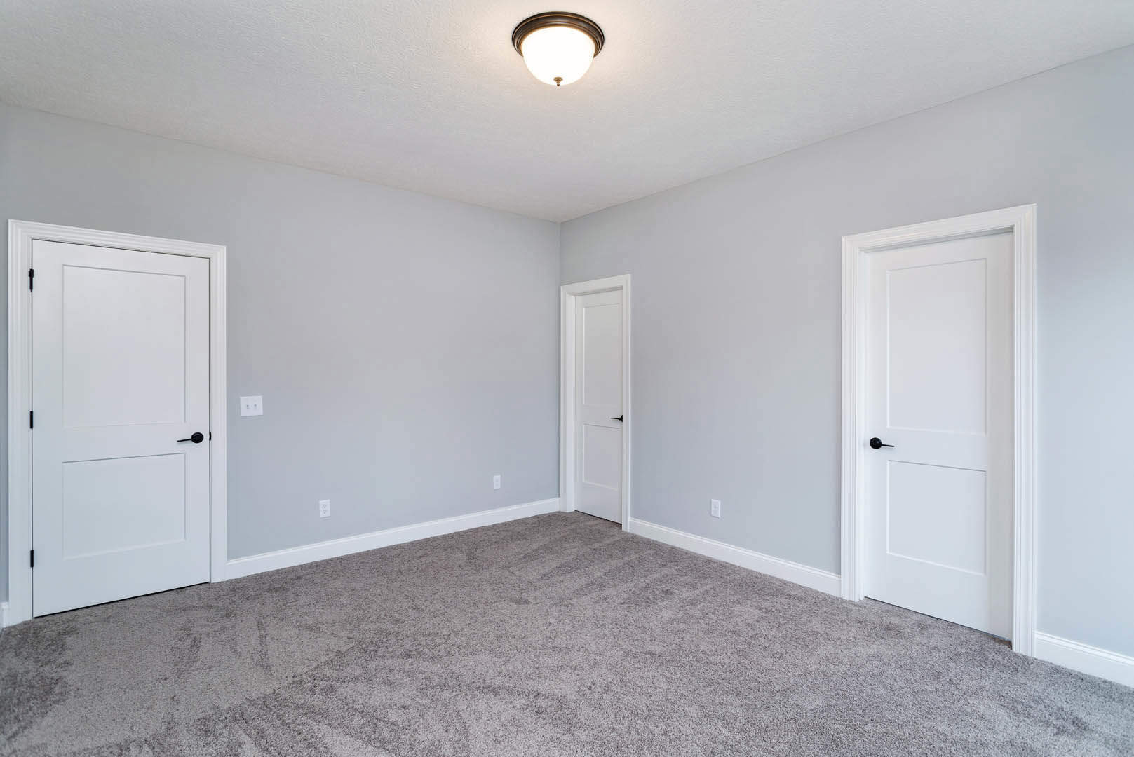 White carpeted room featuring white paneled doors with black handles, ceiling-mounted light fixture, and smooth plaster walls with decorative molding.