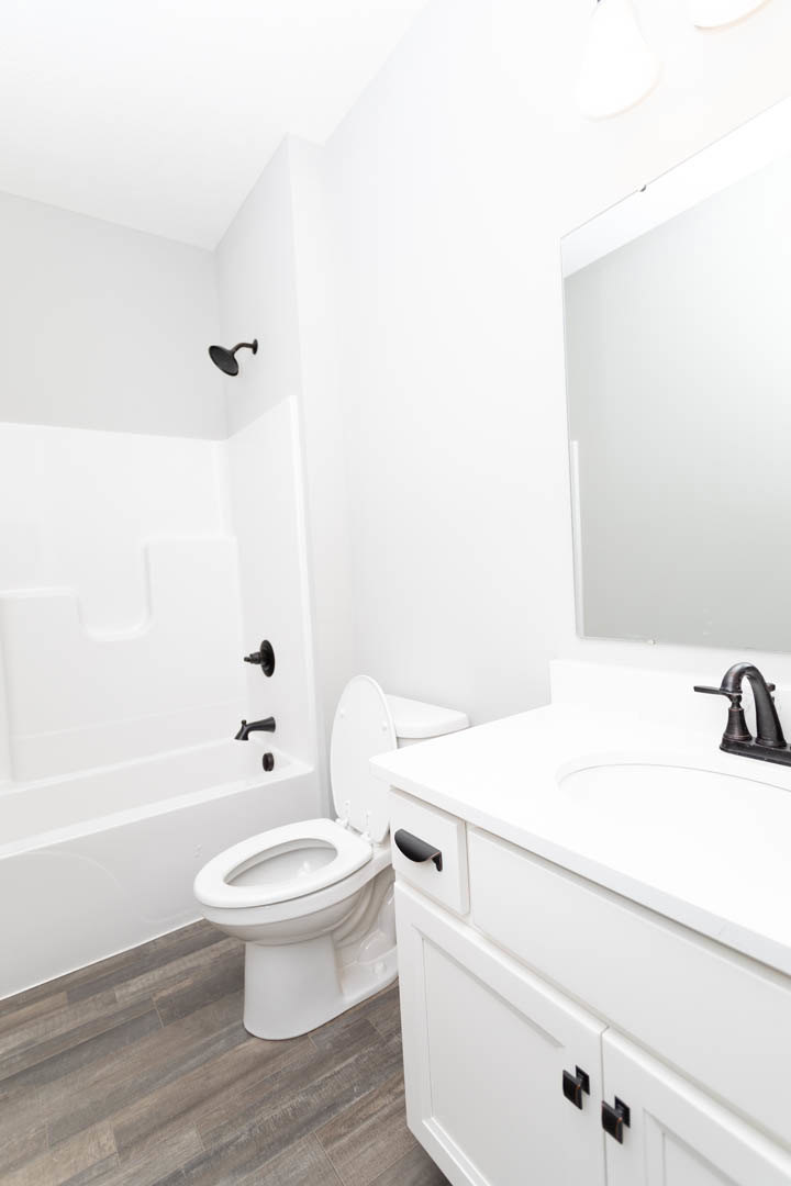 White bathroom featuring a toilet with seat up, rectangular sink with chrome faucet, wood flooring, and white walls and ceiling