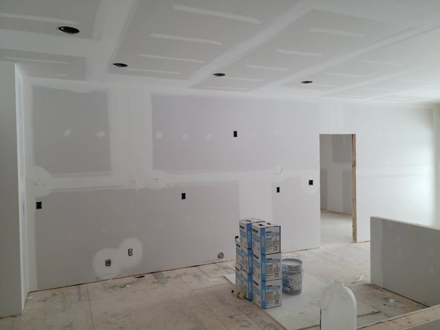 White-walled room with stacked moving boxes on tile floor, white ceramic jug with handle, and plaster walls in a space undergoing renovation.