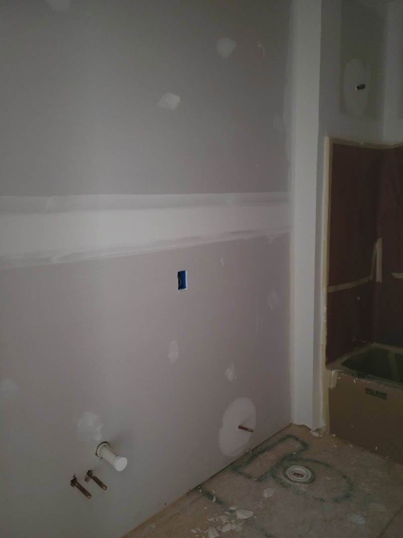 Freestanding white bathtub against smooth plaster wall, chrome faucet, light wood floor, recessed ceiling, modern bathroom remodel