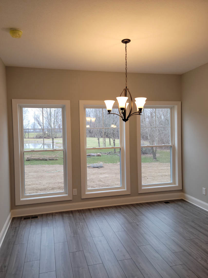 Chandelier with crystal accents hanging from a white ceiling, wood laminate flooring, large windows with views of trees, field, and pond, white walls with crown molding