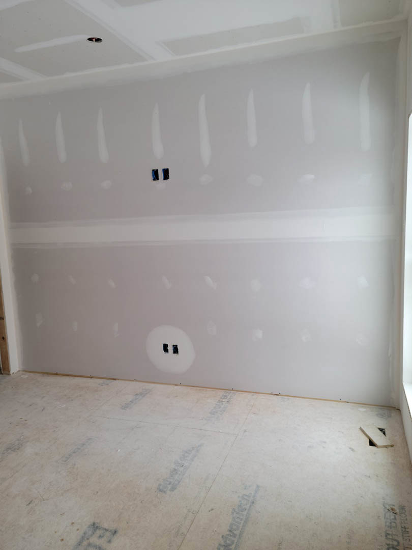 White-walled room with white ceiling, window, smooth white flooring, visible wall outlet, and plaster wall showing small holes.