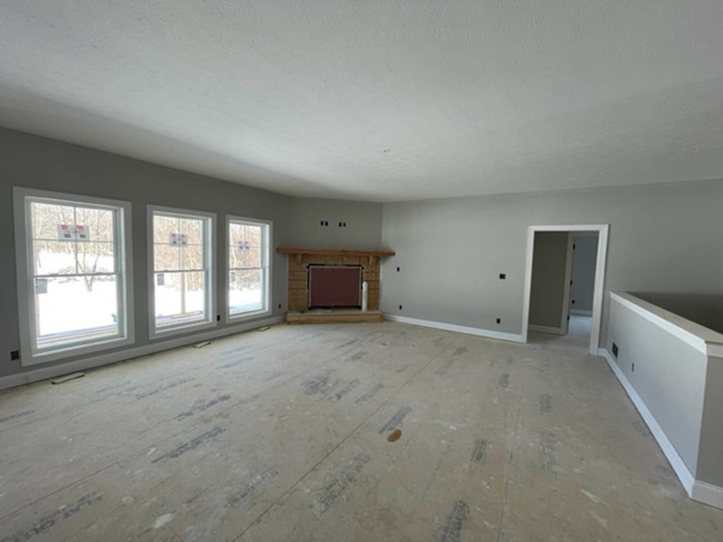 Living room with white walls, laminate flooring, large windows overlooking snowy landscape, modern fireplace with black frame, white baseboards