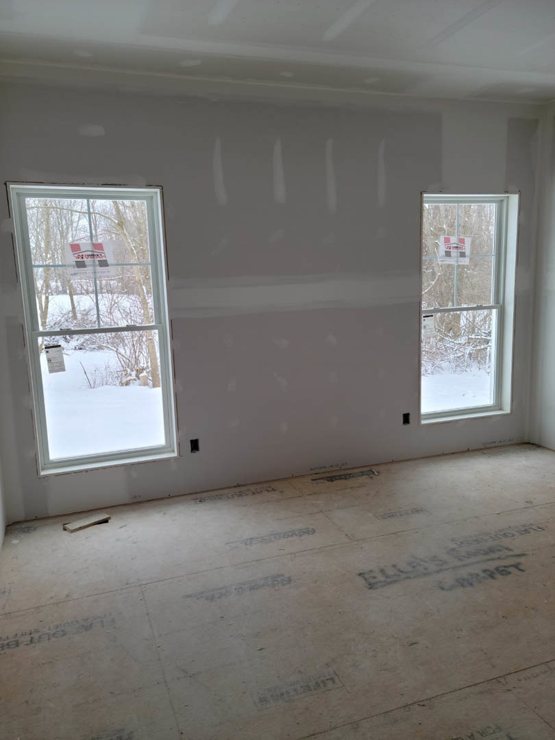 Concrete floor with black writing, large windows facing a snow-covered tree, white plaster walls, ceiling, and a window displaying a sign with red and black text