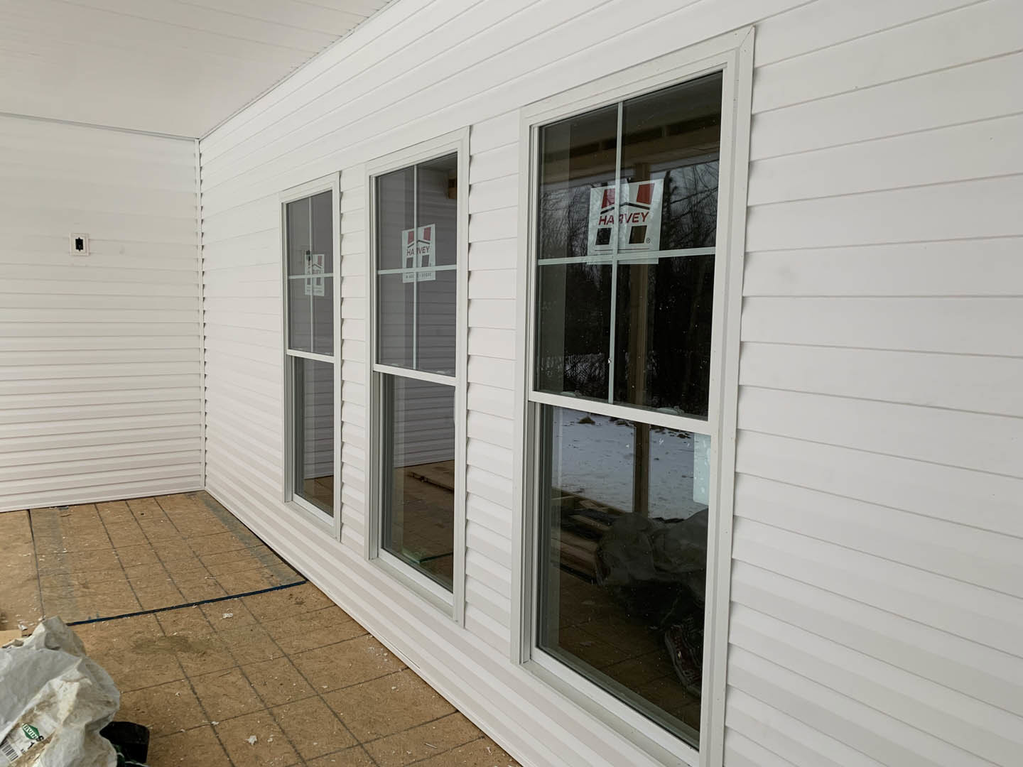 White two-story house with multiple rectangular windows, white trim, and tiled entryway; dirt landscaping with a white bag and a white sign with red text near the front.