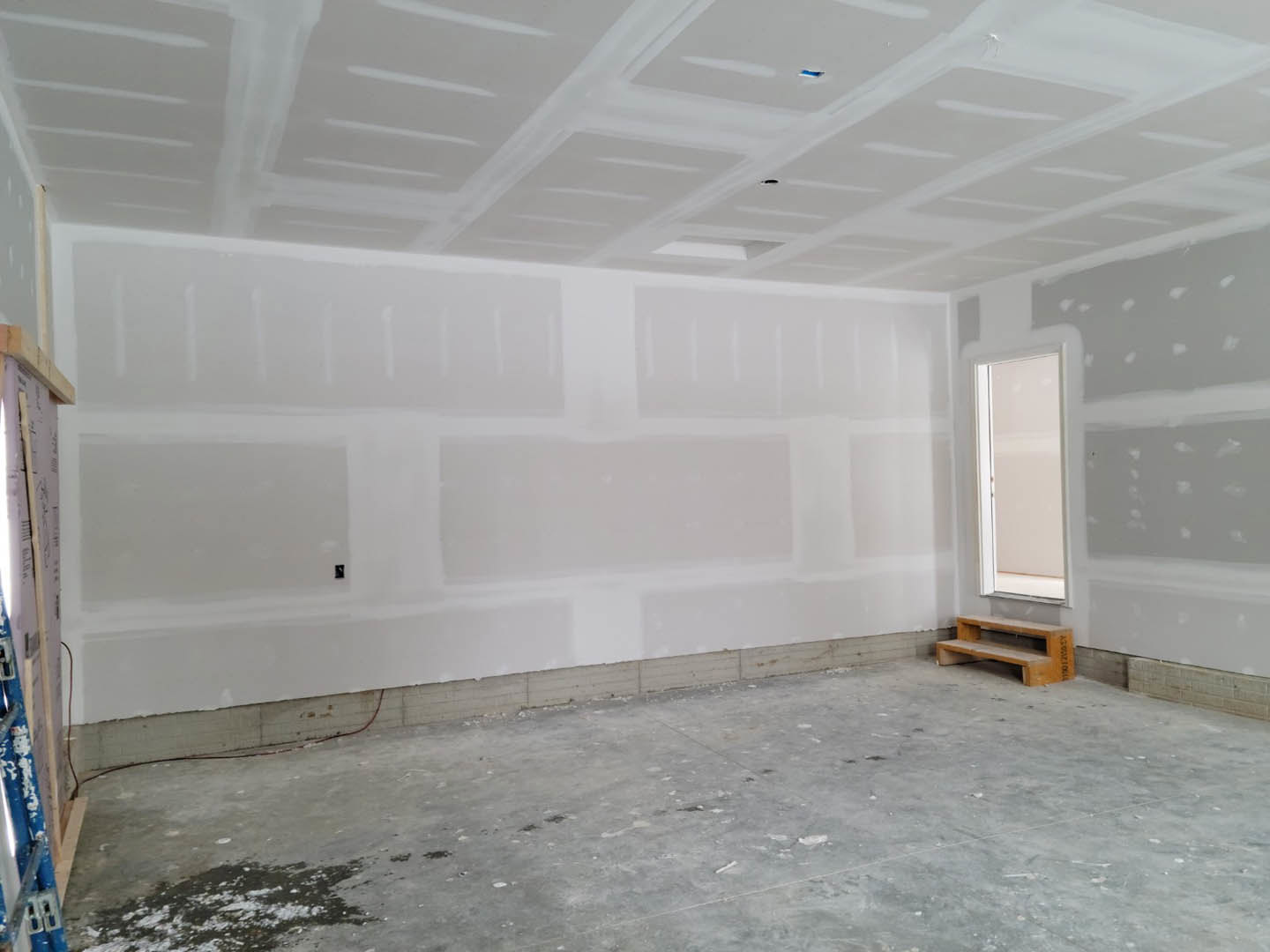 White-walled room with a large window, concrete floor, wooden bench with steps, and white ceiling featuring recessed holes