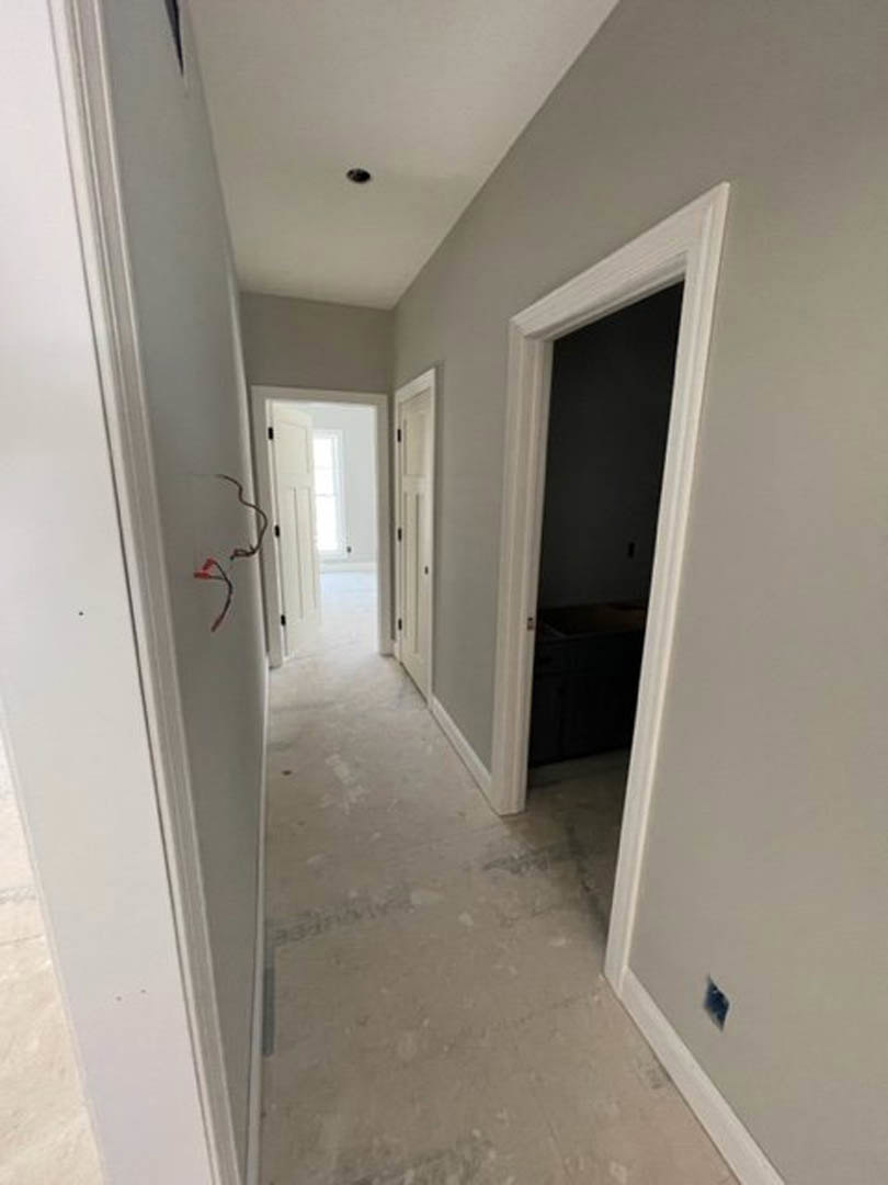 Hallway with white painted walls and white trim, white door with window, dark accent wall visible through doorway, exposed wires on white wall, light-colored flooring