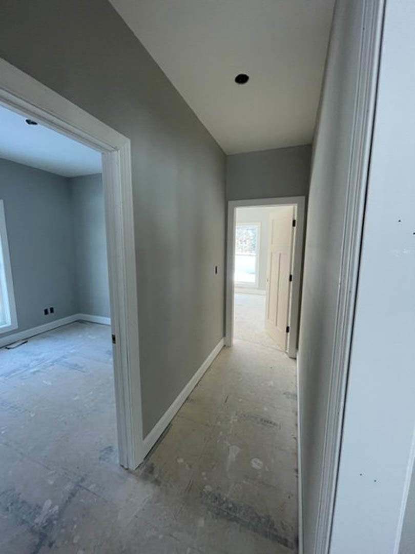 Hallway with smooth white plaster walls, white door featuring a window and black hinges, light wood flooring, and white ceiling