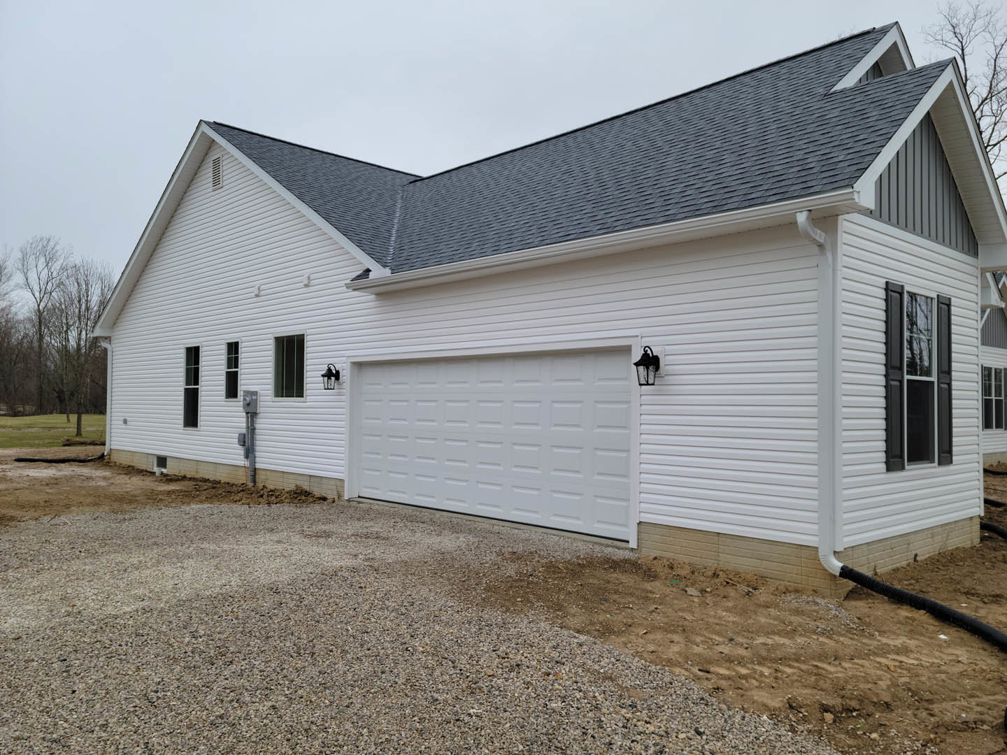 White siding house with attached garage, paneled garage door, double-hung windows, gable roof, and landscaped front yard with trees.