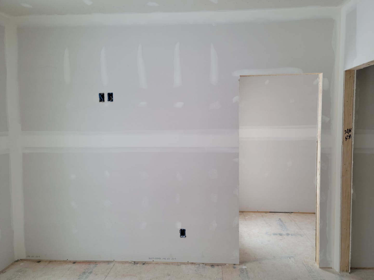 White plaster wall with a square cutout, adjacent to a closed door with white trim, light-colored flooring, and neutral ceiling visible in a modern interior room.