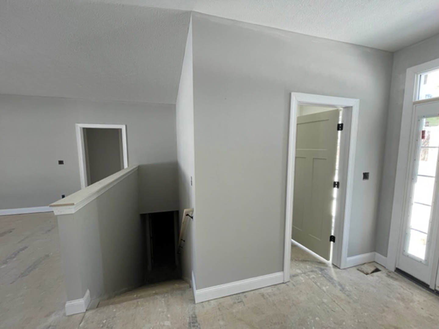 Open living space featuring a wooden staircase with white risers, multiple white doors, light streaming through a doorway, white plaster walls, and hardwood flooring