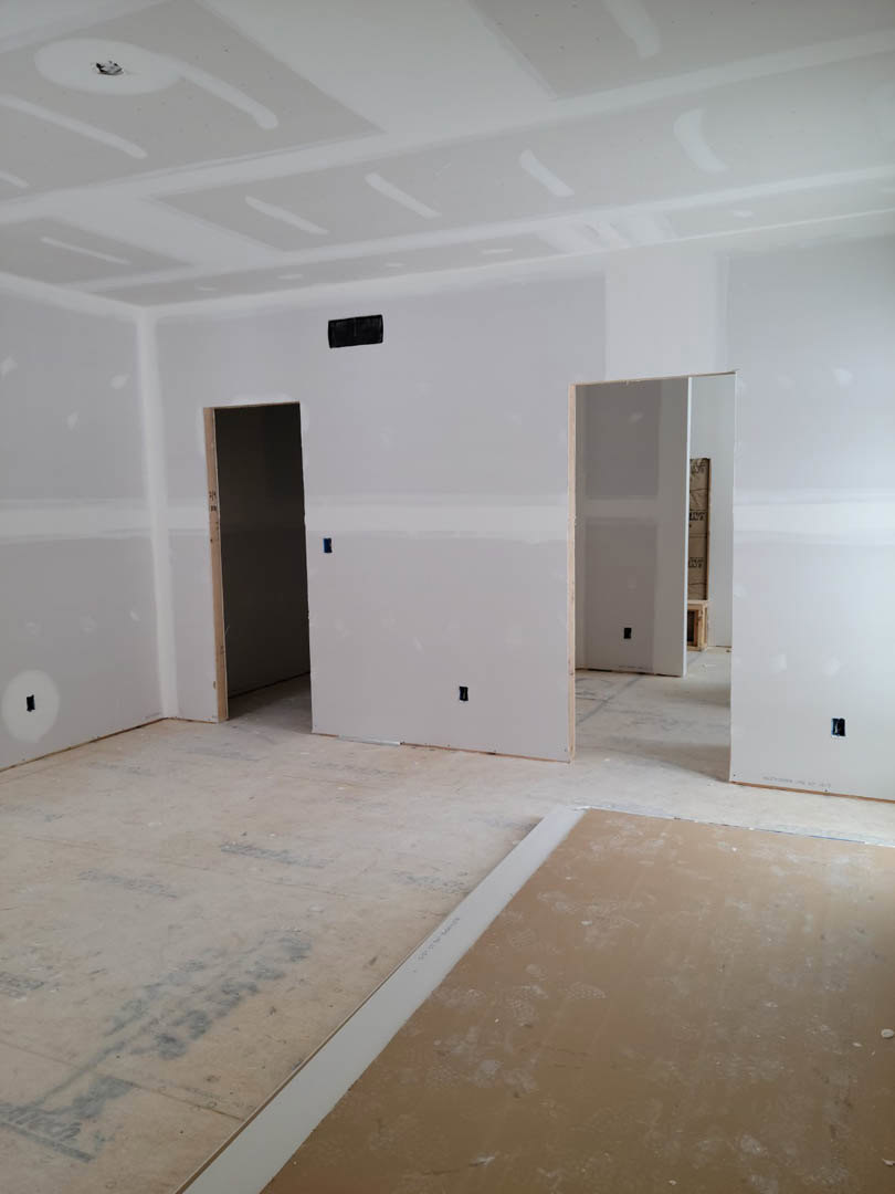 White-walled room with tile flooring, white door, and plaster ceiling; small box near door and black object on white surface.