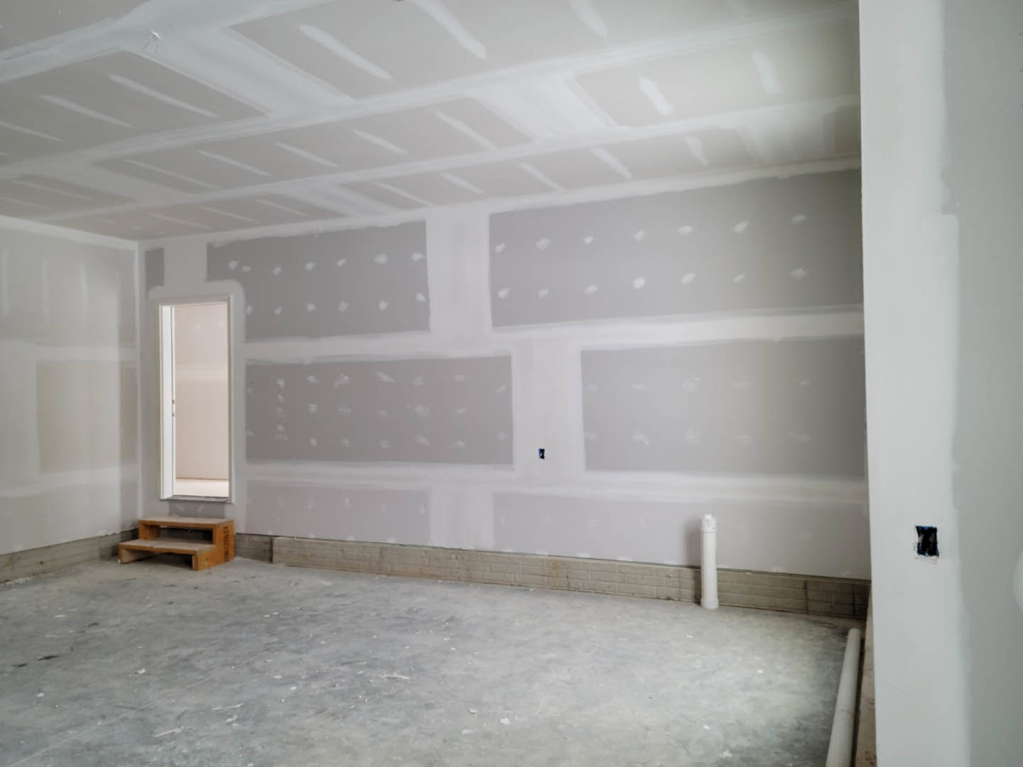 White-painted room with a brick accent wall, large window, wooden step stool, white floor, and white ceiling.