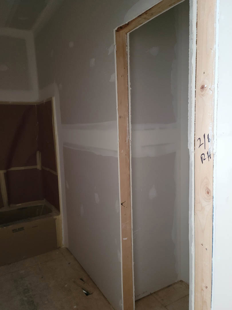 White-painted walls and wood beam in a bathroom with a freestanding tub, light flooring, and a door; cardboard box sits in the corner.