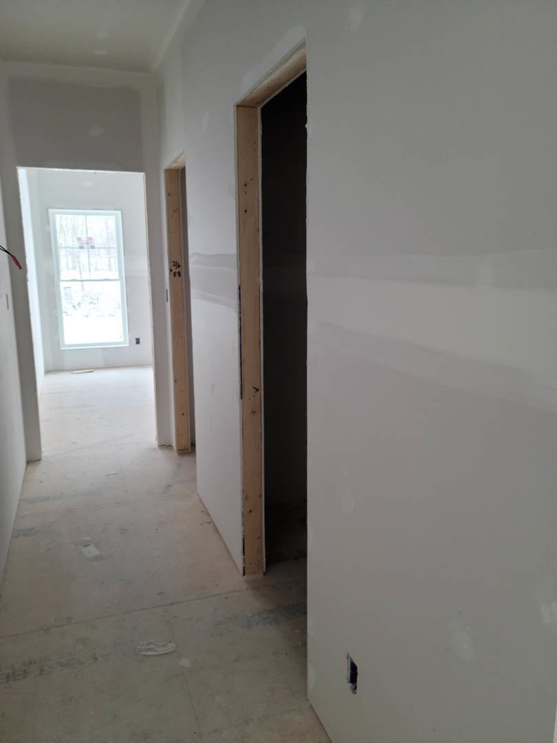 Hallway with smooth white plaster walls, light wood flooring, open doorway, and window overlooking snowy landscape