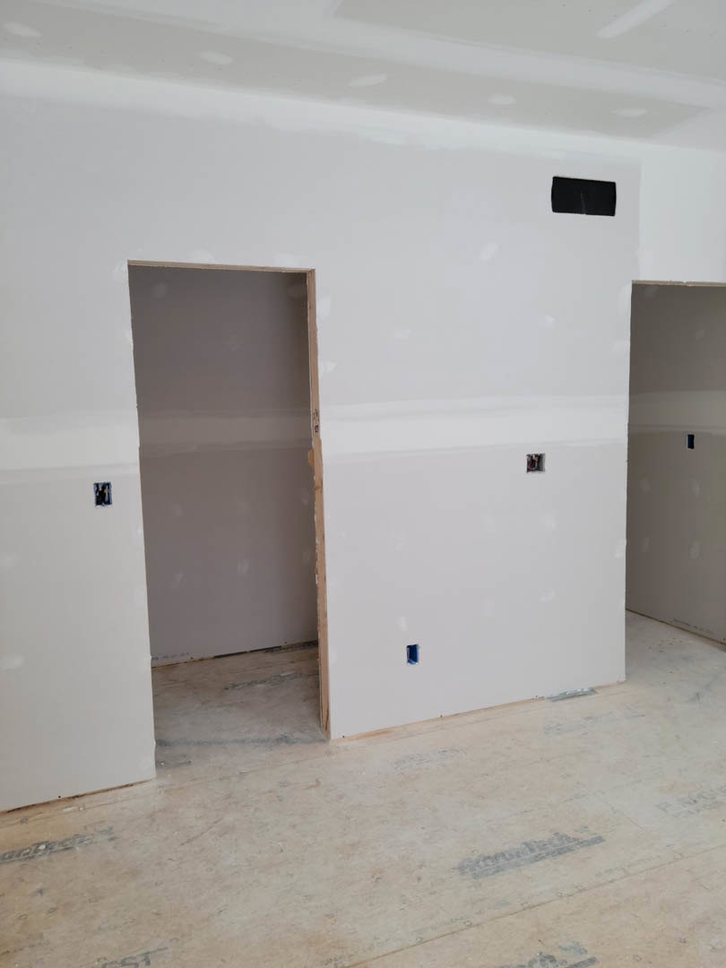 Open door leading into unfinished room with plywood flooring, white plaster walls, and visible hole in wall.