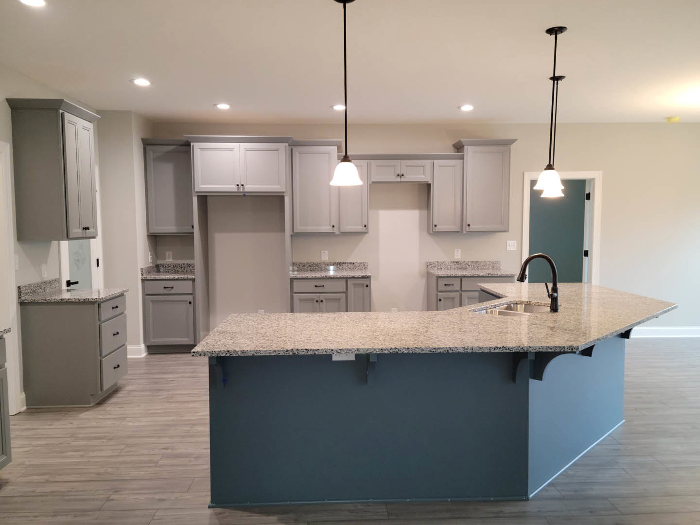 Granite kitchen island with built-in drawers, white cabinetry, stainless steel sink, black hardware, and white doors in a modern interior.