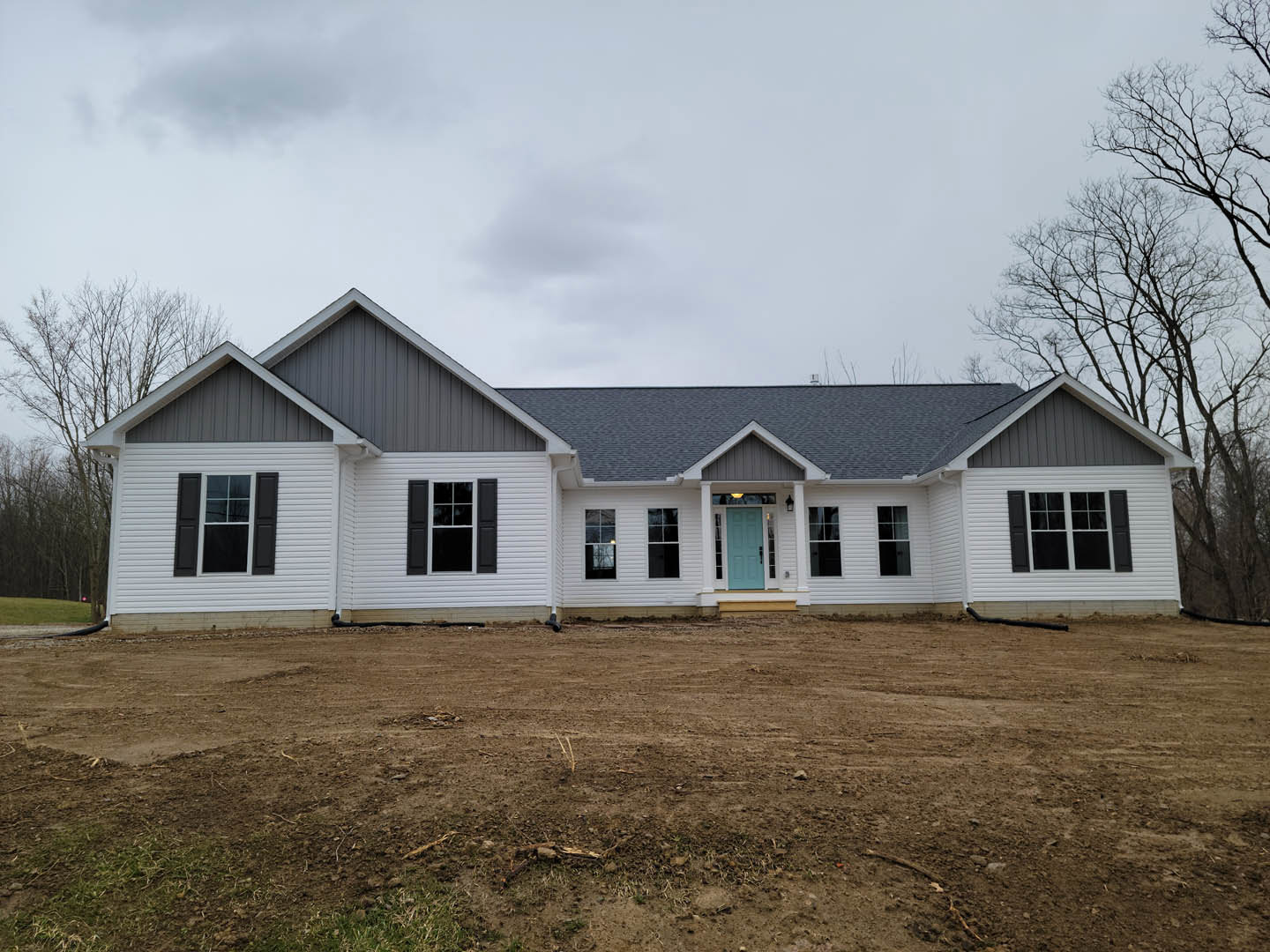 White house with black shuttered windows, blue front door, and dirt yard under partly cloudy sky