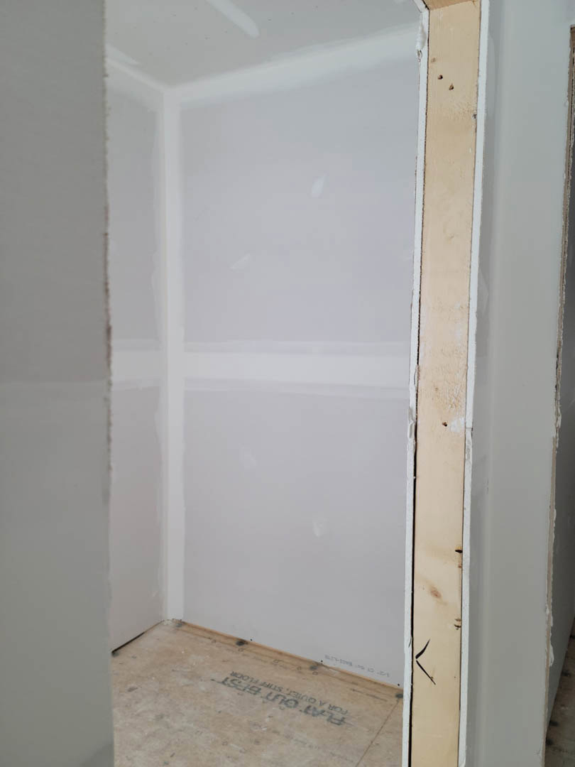 White painted wall with a black trim line, light-colored floor, and an open doorway leading to another room