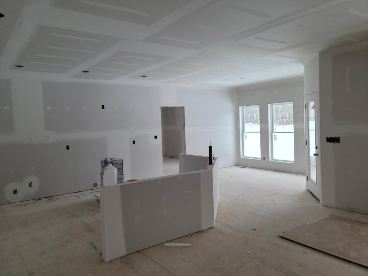 White plaster walls with a white jug on the floor, light switches, and two windows; wooden flooring and a square fixture mounted on the wall.